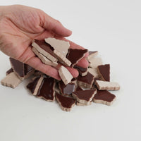 Video of Flip XL ceramic puzzle pieces in mocha, opaque glazed porcelain, 20–60 mm, picked up from a pile by hand and dropped back to show their size, shapes and finish