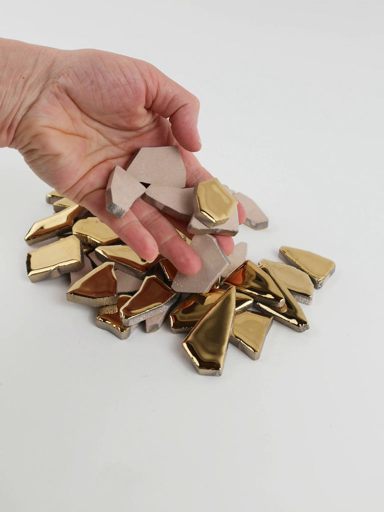 Video of Flip XL ceramic puzzle pieces in gold, opaque glazed porcelain, 20–60 mm, picked up from a pile by hand and dropped back to show their size, shapes and finish